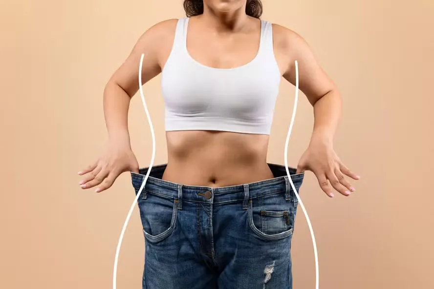 Mulher vestindo uma calça jeans em número muito maior, mostrando resultado de emagrecimento